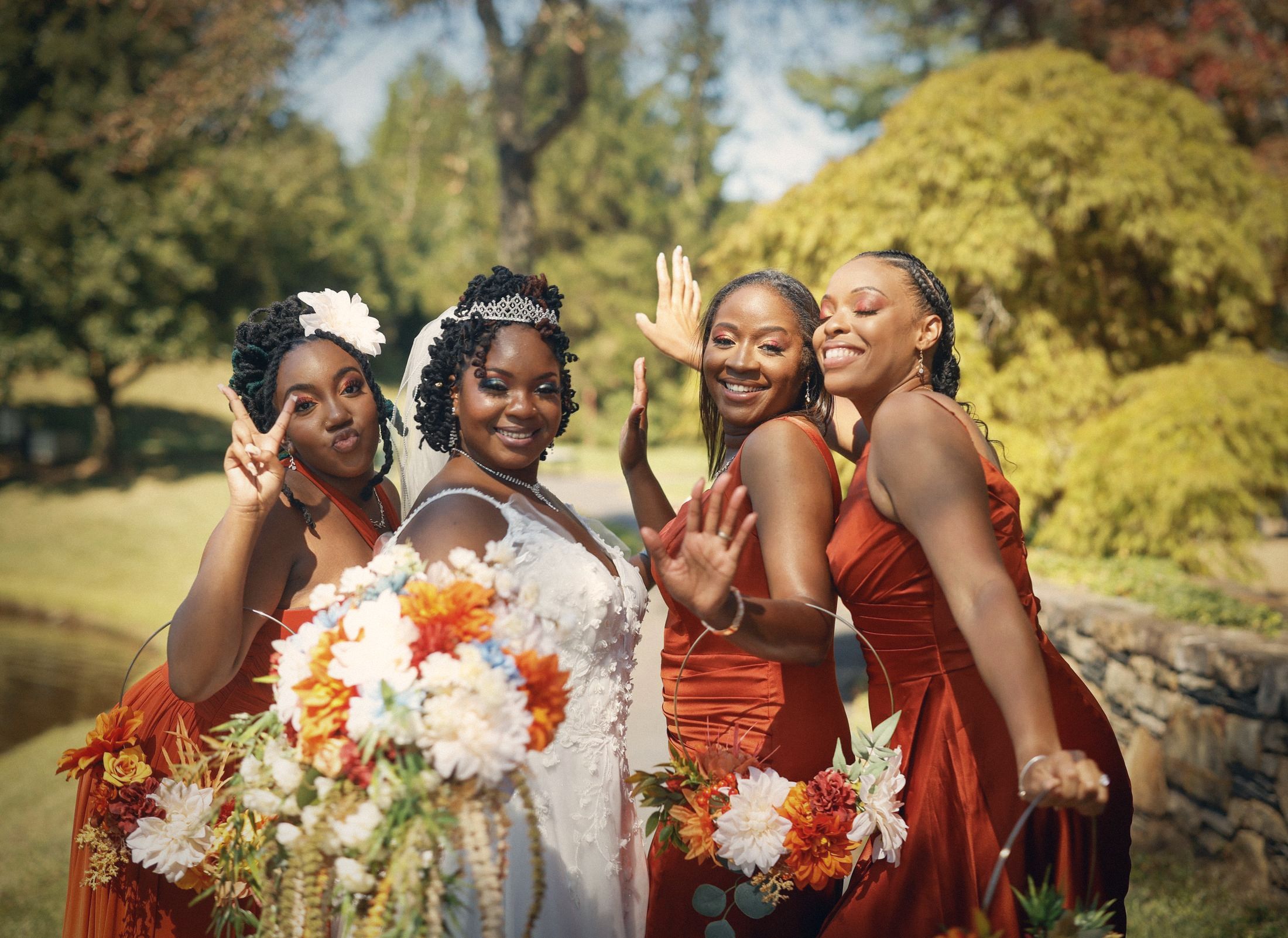 Bride and bridesmaids in rust satin dresses posing in a garden