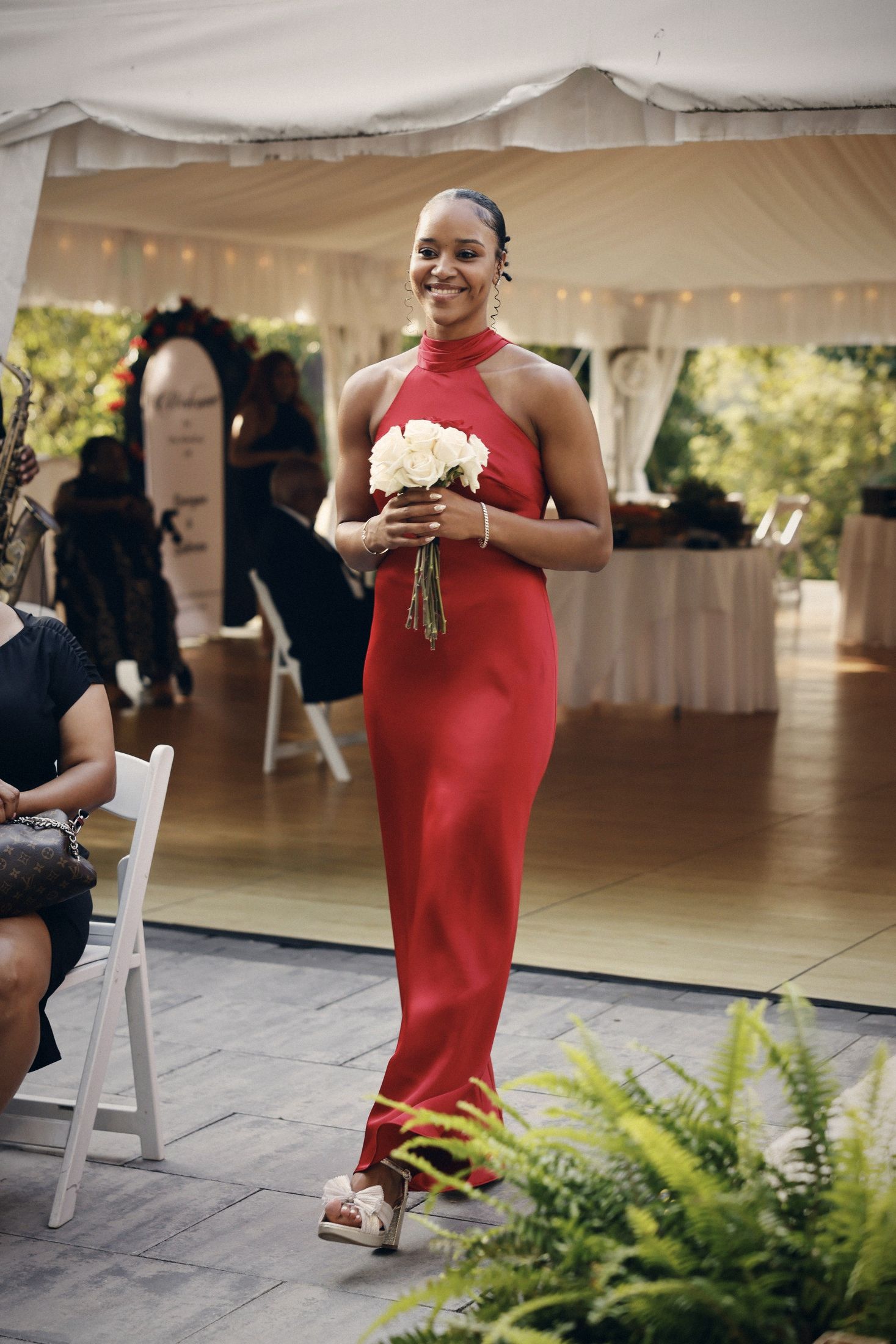 Bridesmaid in a red gown walking in with white roses