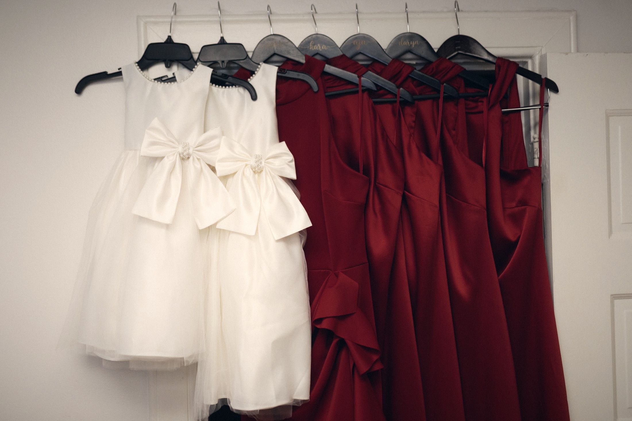 Flower girl dresses and red bridesmaid dresses on hangers