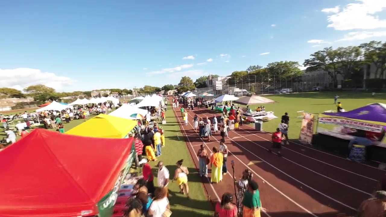 Low aerial pass over festival vendor tents on a running track