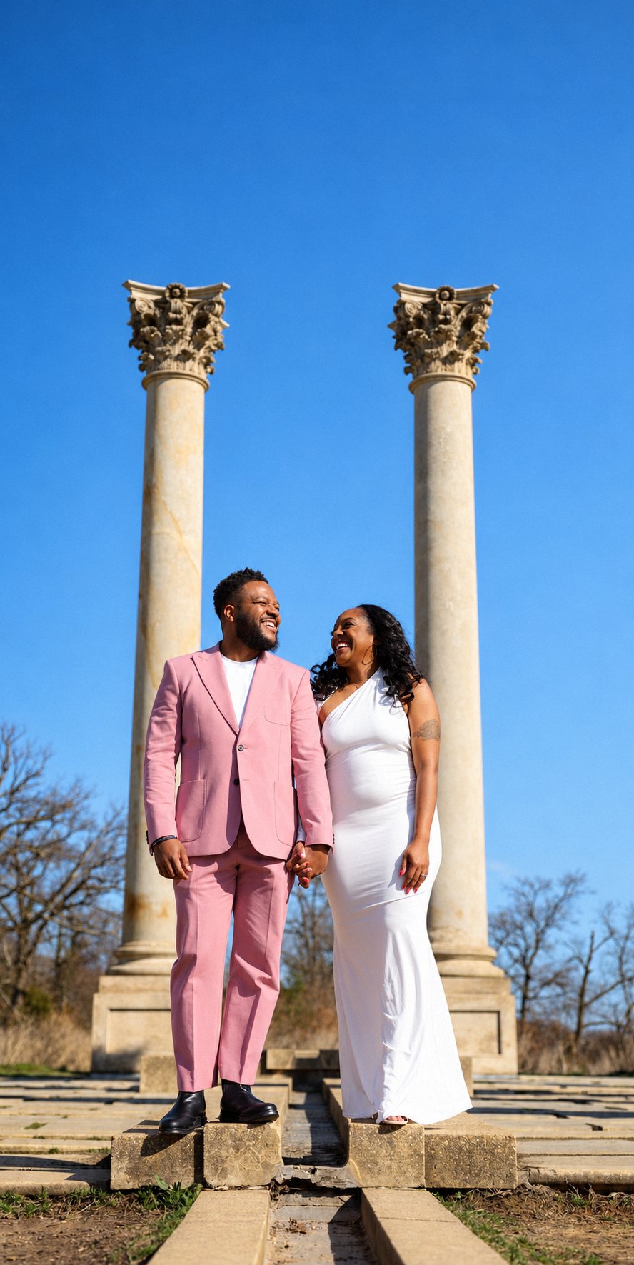 Engaged couple laughing and holding hands between marble columns