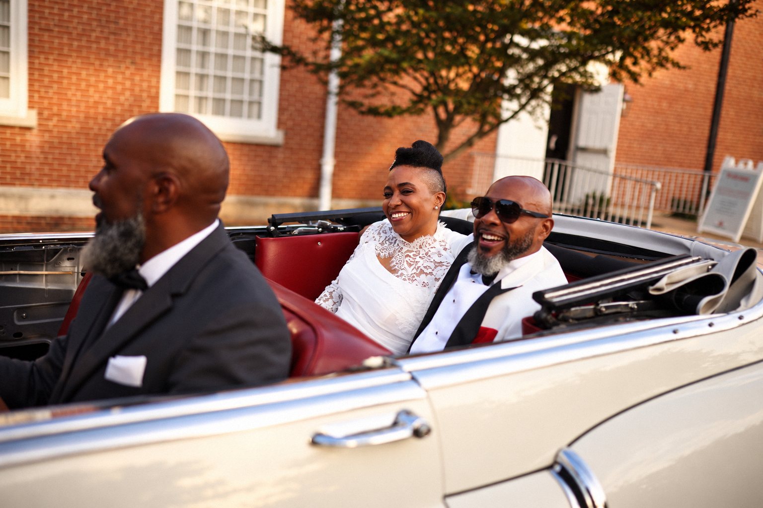 Newlyweds laughing in the back of a vintage convertible