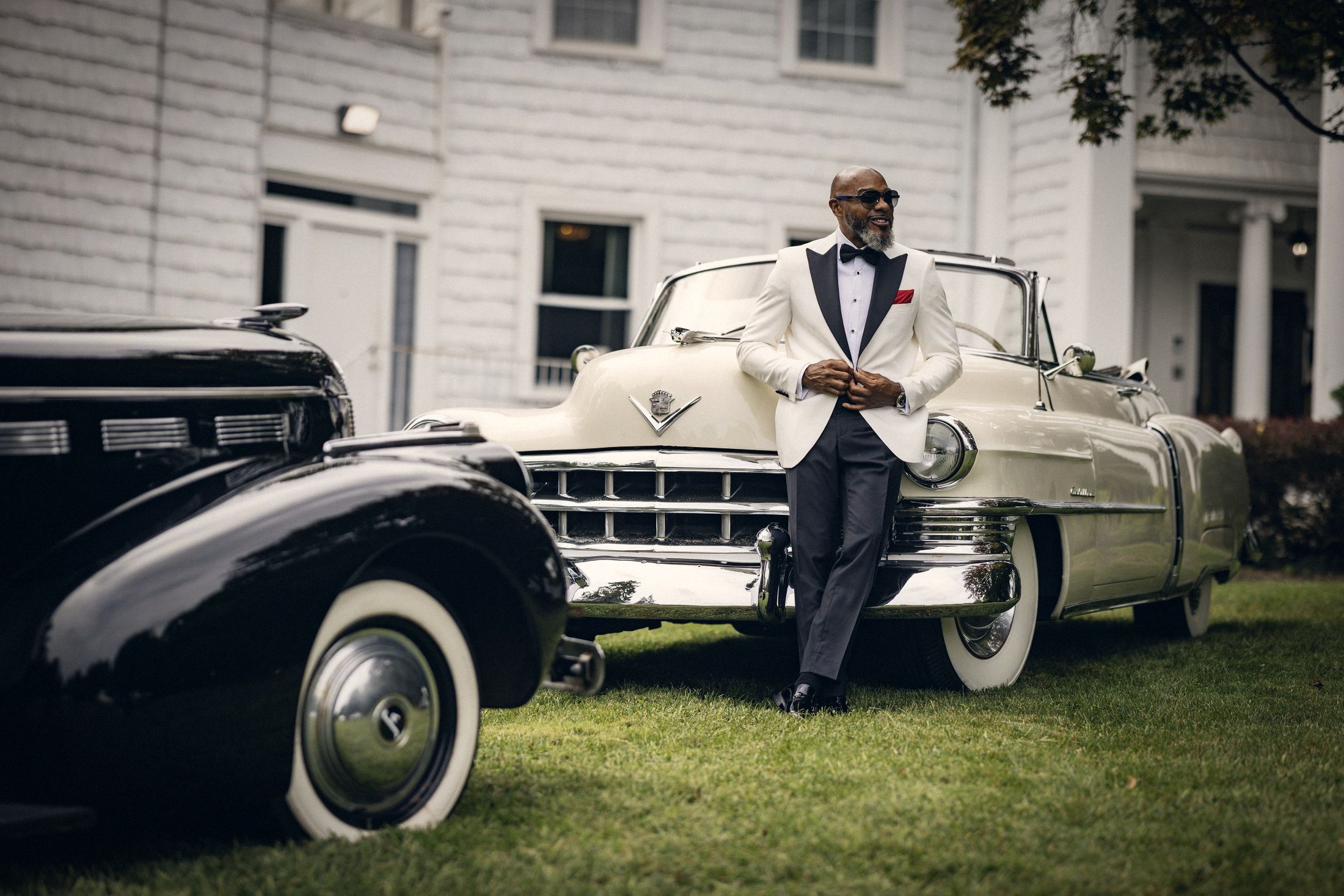 Groom in a white dinner jacket leaning on a vintage convertible