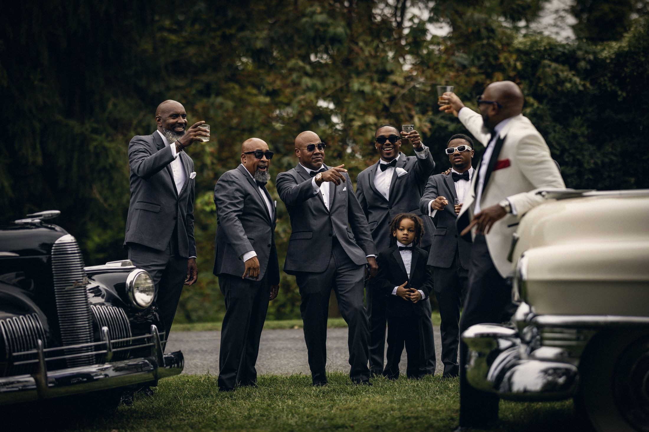 Groomsmen raising a toast beside vintage cars