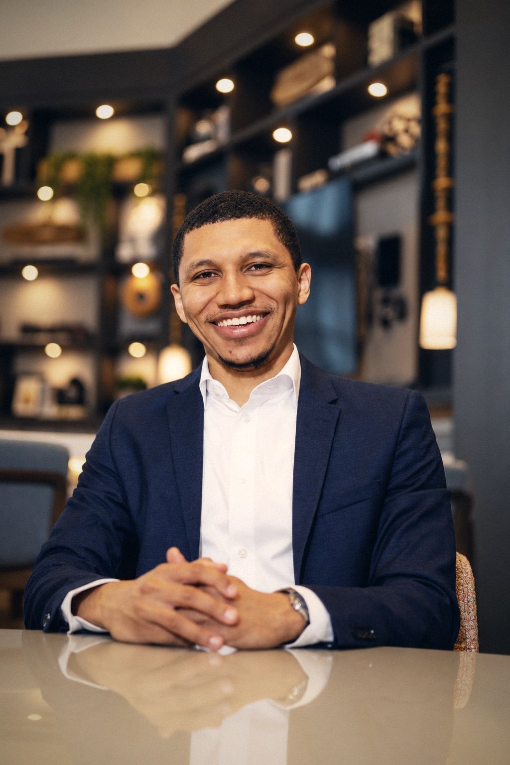Smiling man in a navy blazer seated at a table in a warm lounge