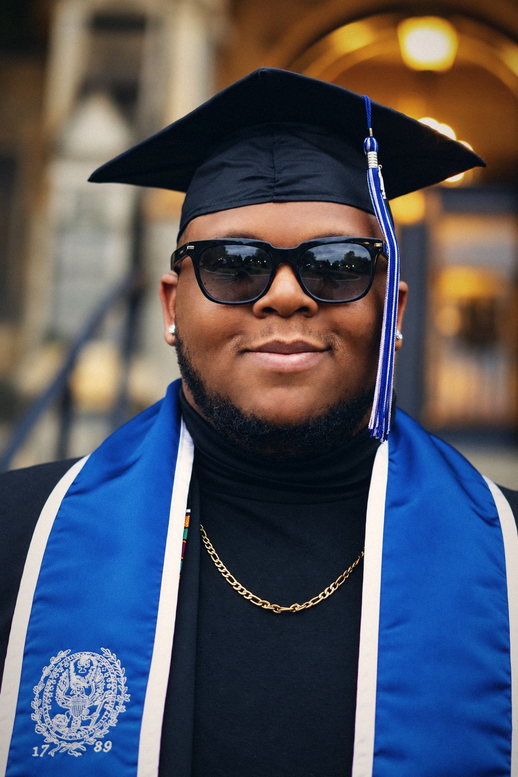 Graduate in sunglasses with a blue and white stole and gold chain