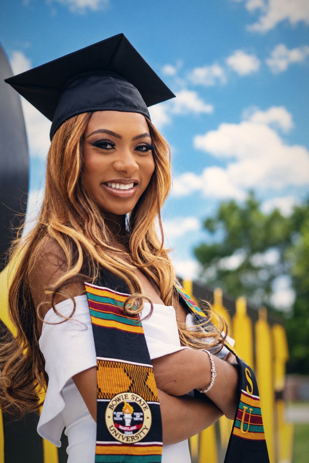 Bowie State graduate in cap and kente stole smiling with arms crossed