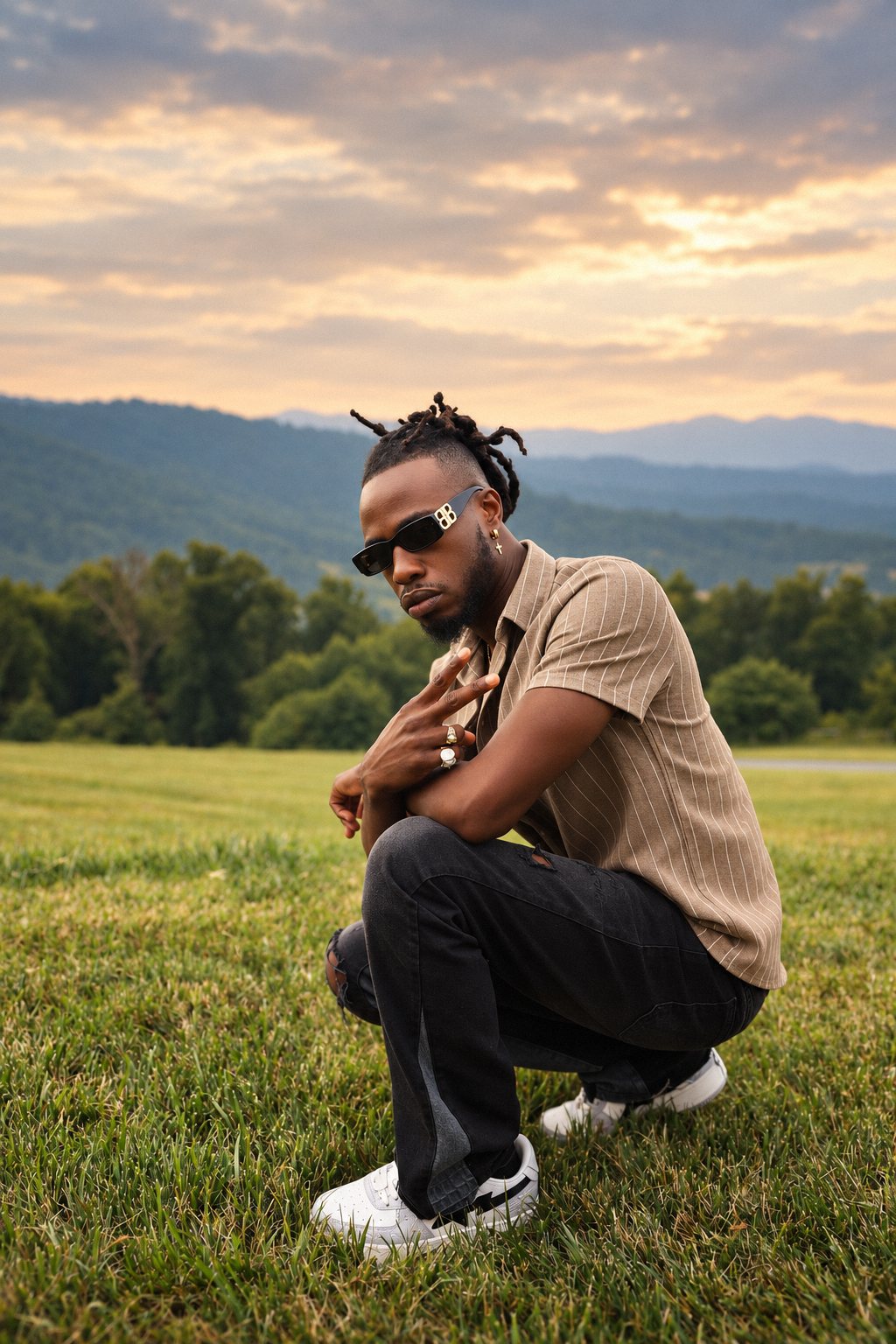 Man in a pinstripe shirt crouched in a field with mountains behind him at sunset