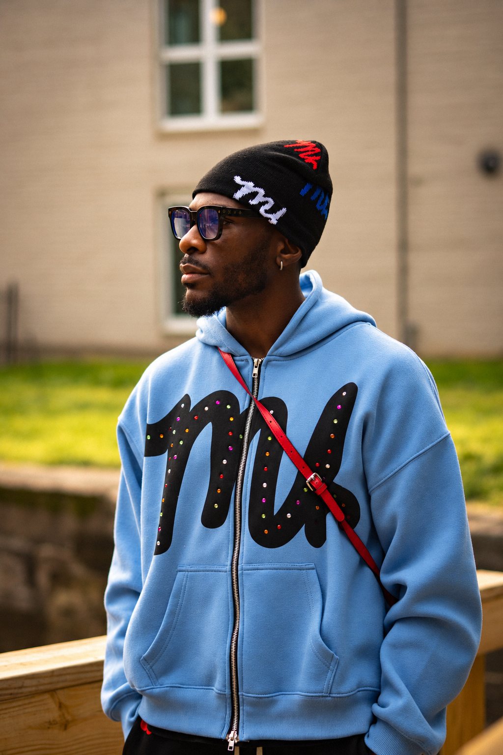 Man in a beanie and blue hoodie with a red crossbody strap