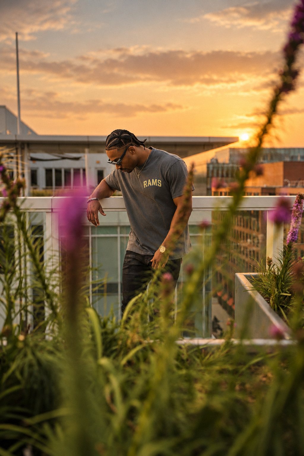 Man leaning on a rooftop railing at sunset framed by purple flowers