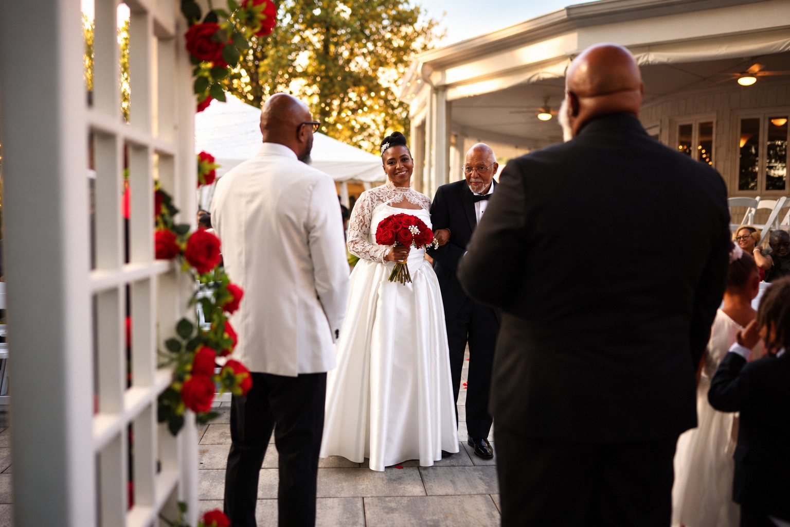 Bride and her father walking toward the groom, seen past the rose arch