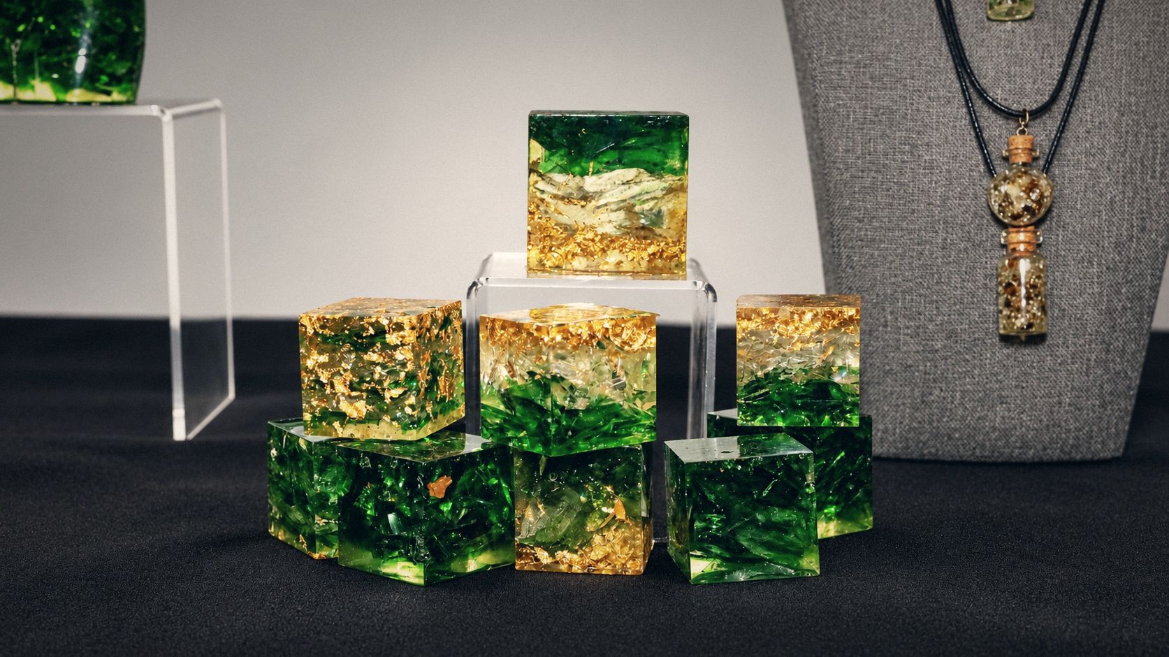 Green and gold resin cubes on an acrylic display beside pendant necklaces