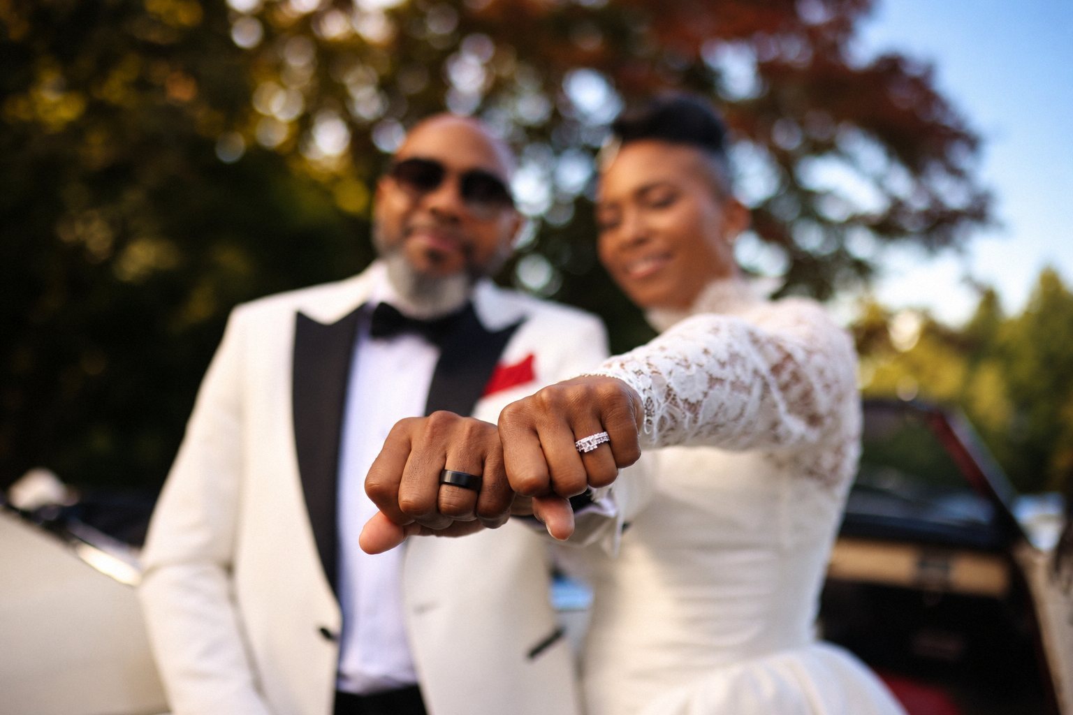 Bride and groom showing their wedding rings in front of a vintage car