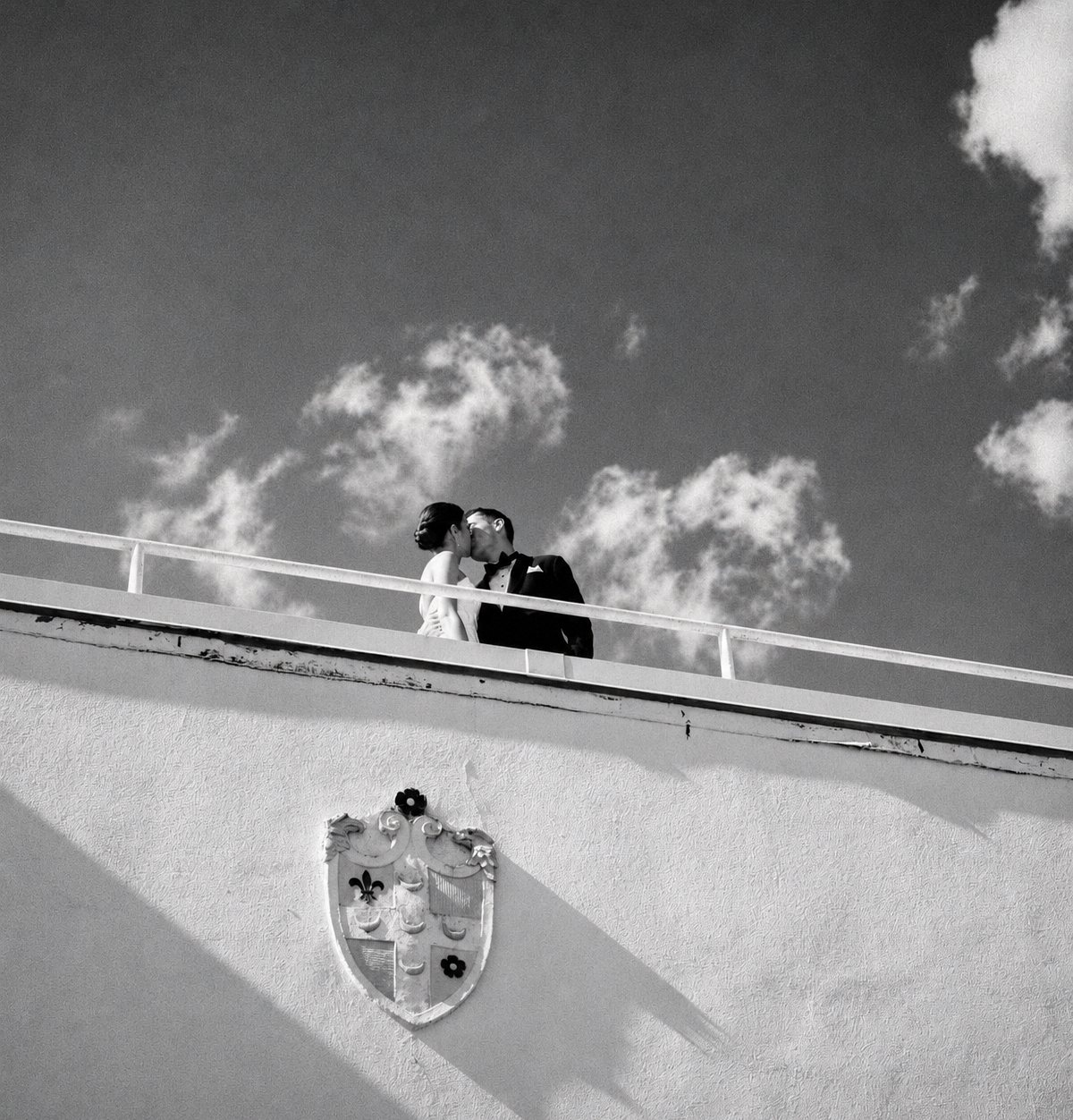 Black and white photo of a couple kissing on a rooftop against the sky