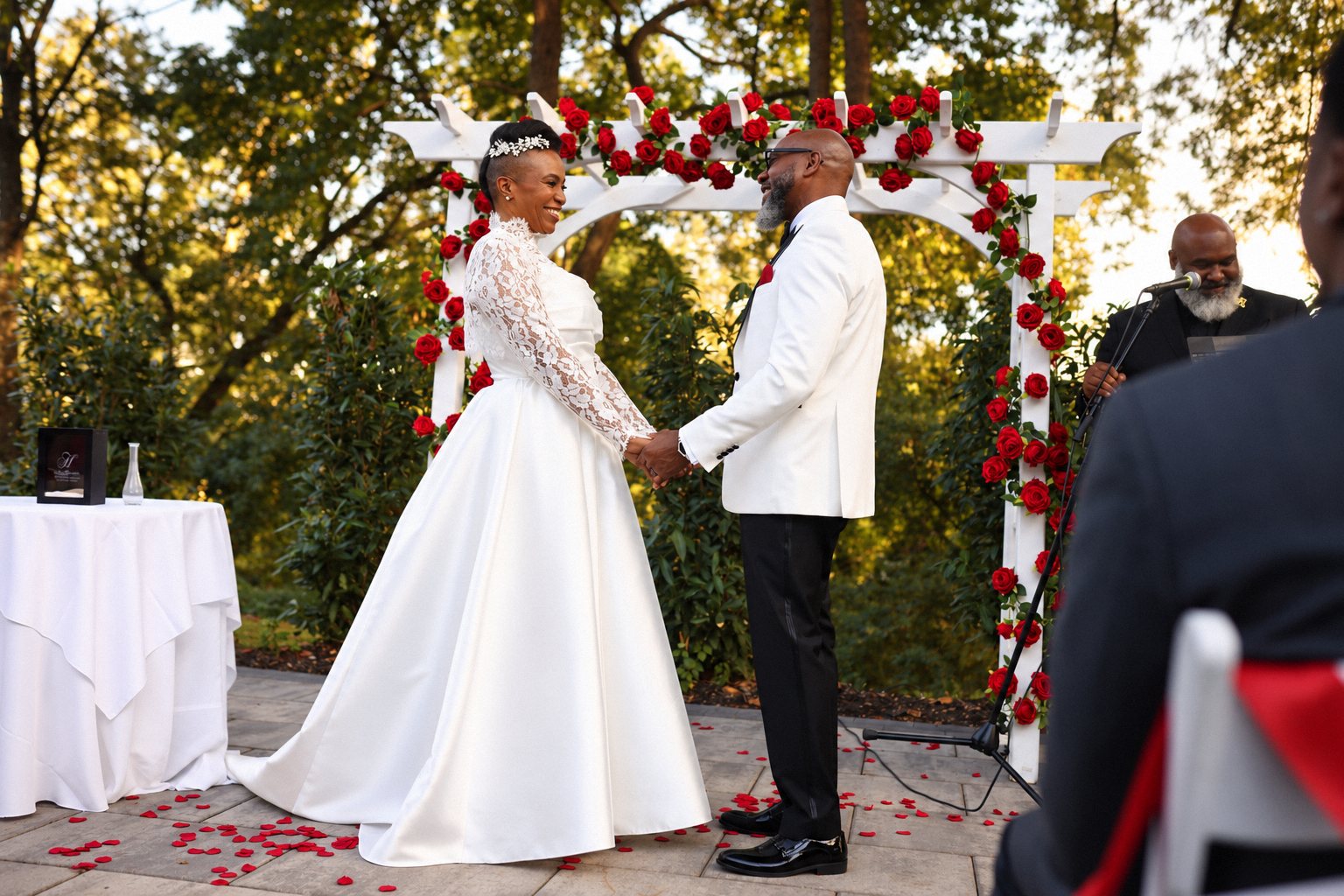 Bride and groom smiling and holding hands under a red rose arch