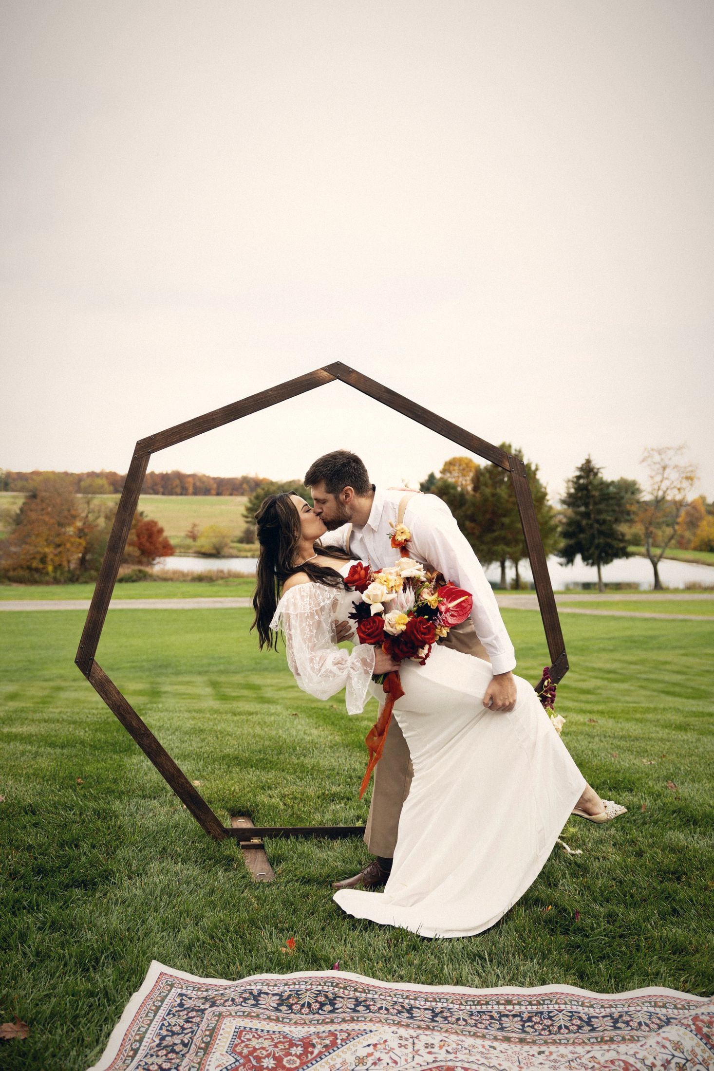 Groom dips bride for a kiss inside a wooden ceremony arch