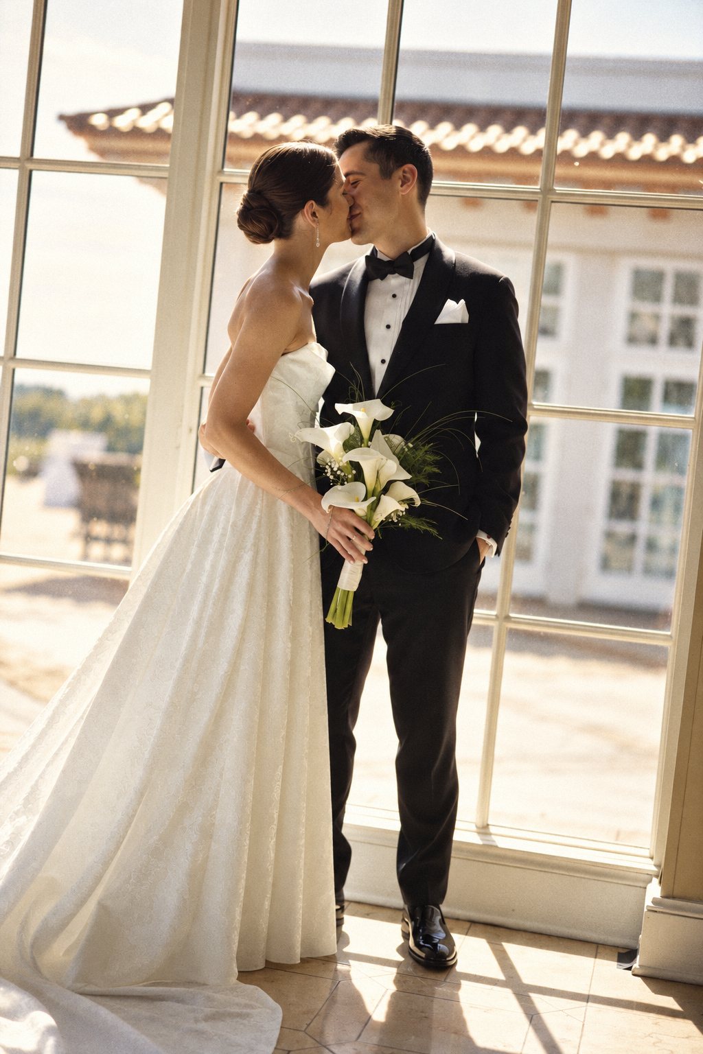 Bride and groom kissing by tall windows