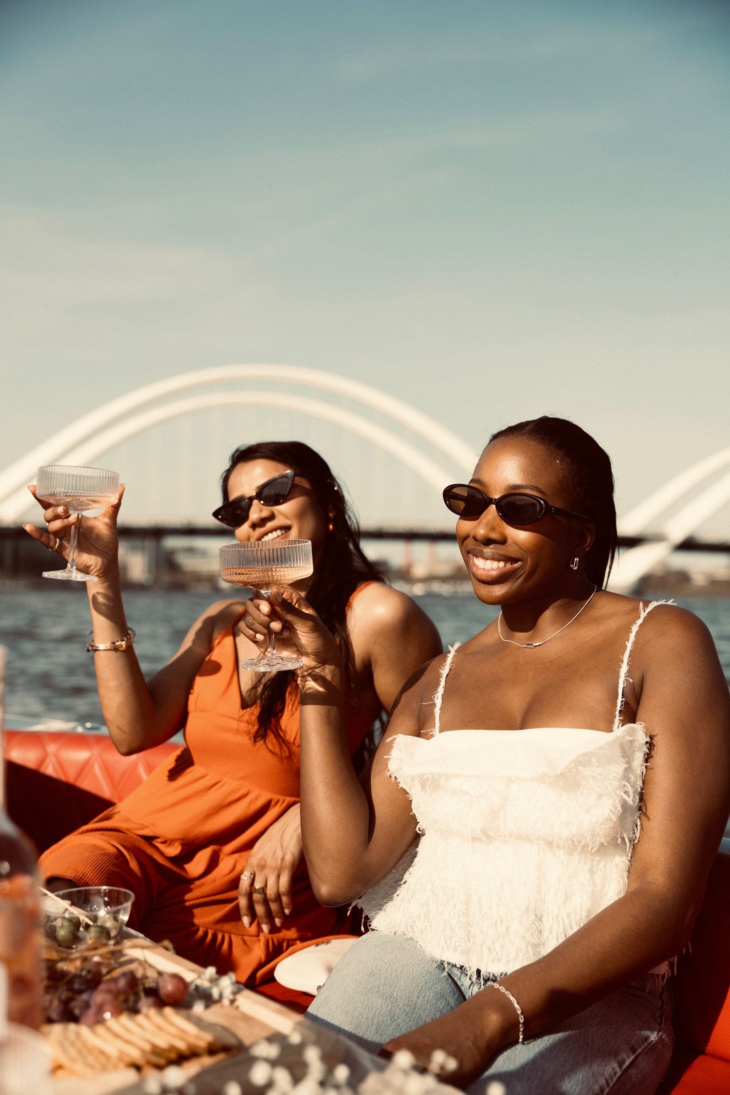 Two friends raising glasses on a boat with the Frederick Douglass Bridge behind them